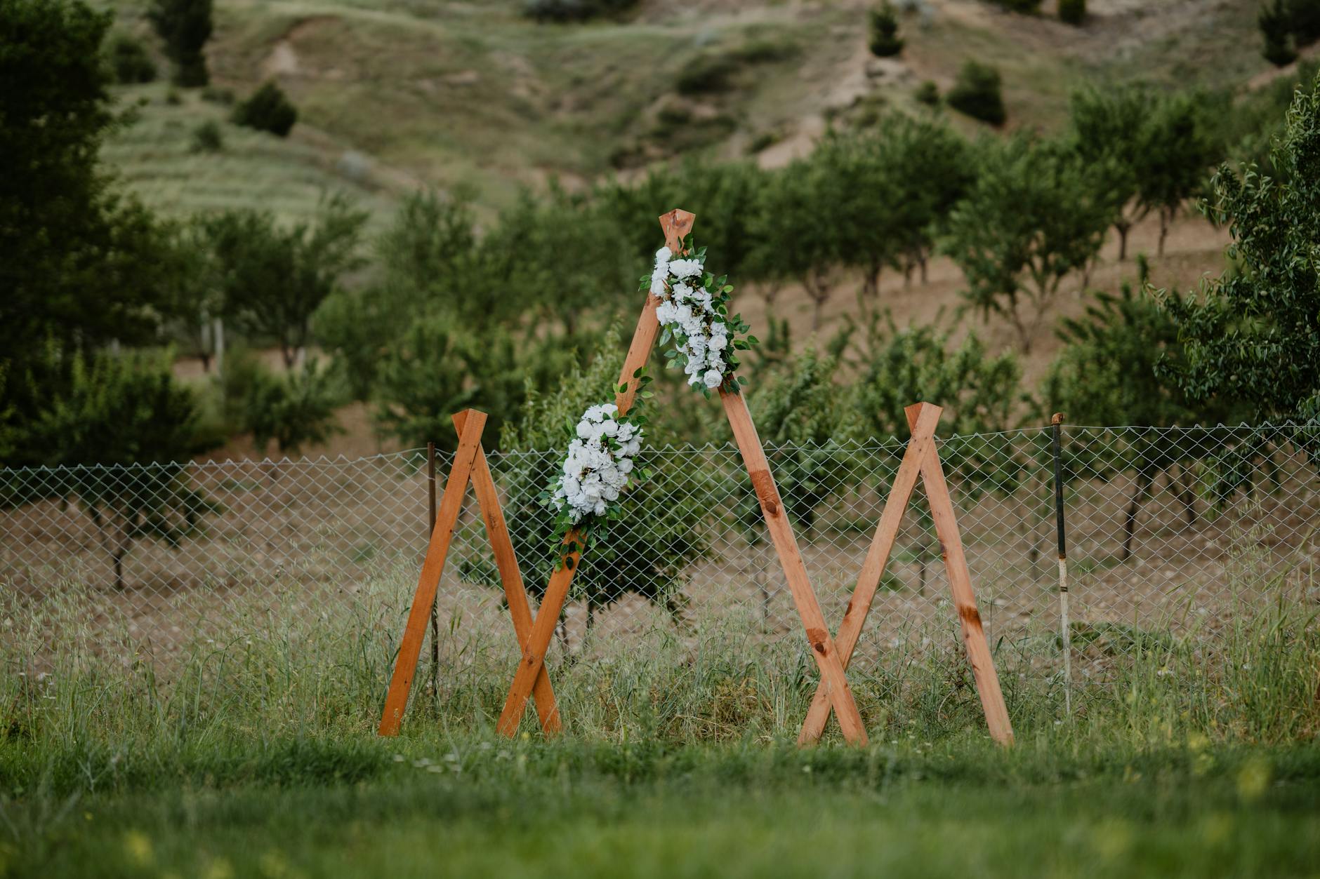 Drewniany ślubny łuk z białymi kwiatami w plenerze