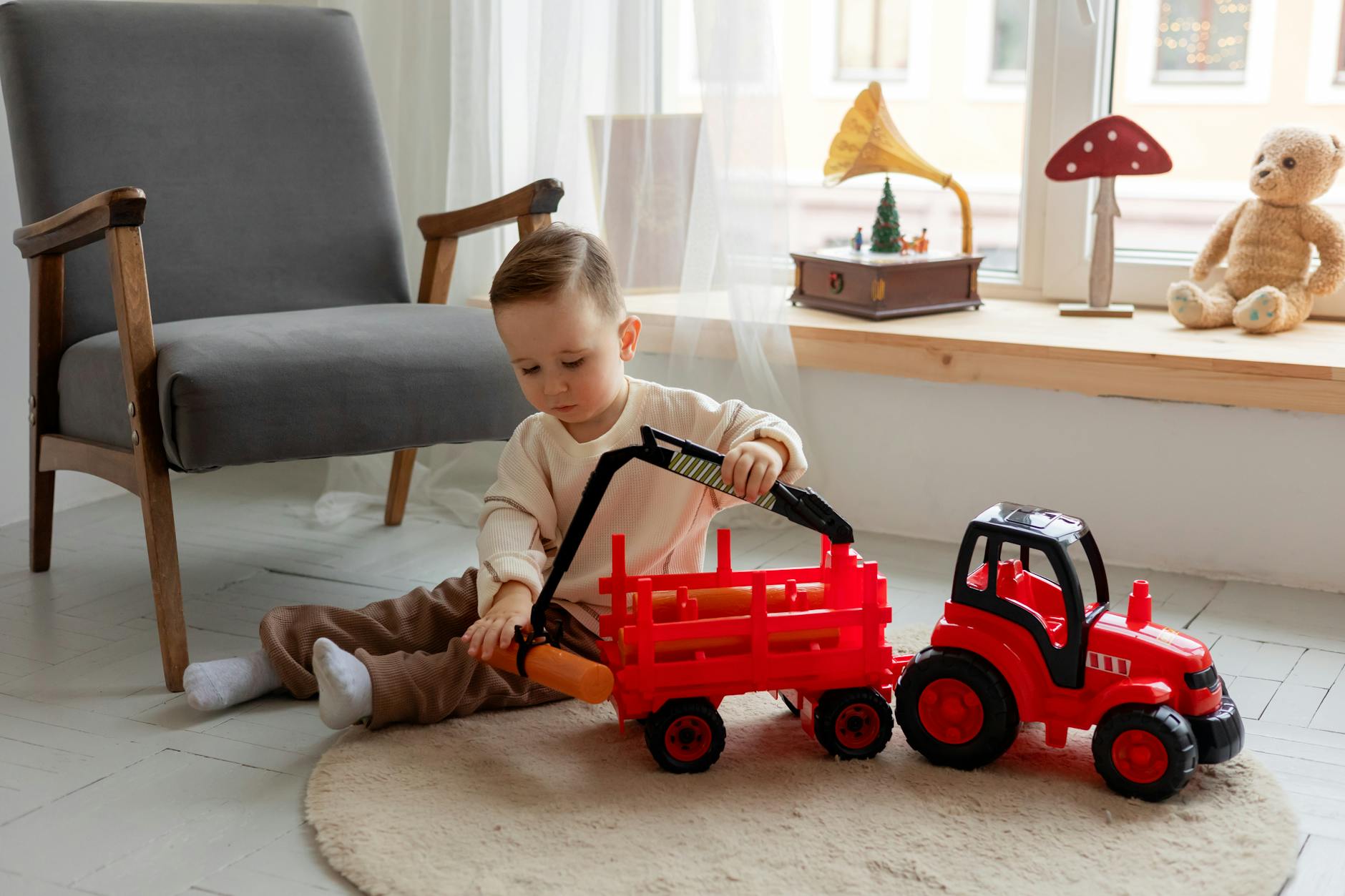 Dziecko bawi się czerwonym traktorkiem zabawką w przytulnym pokoju Dziecko bawi się czerwonym traktorkiem zabawką w przytulnym pokoju