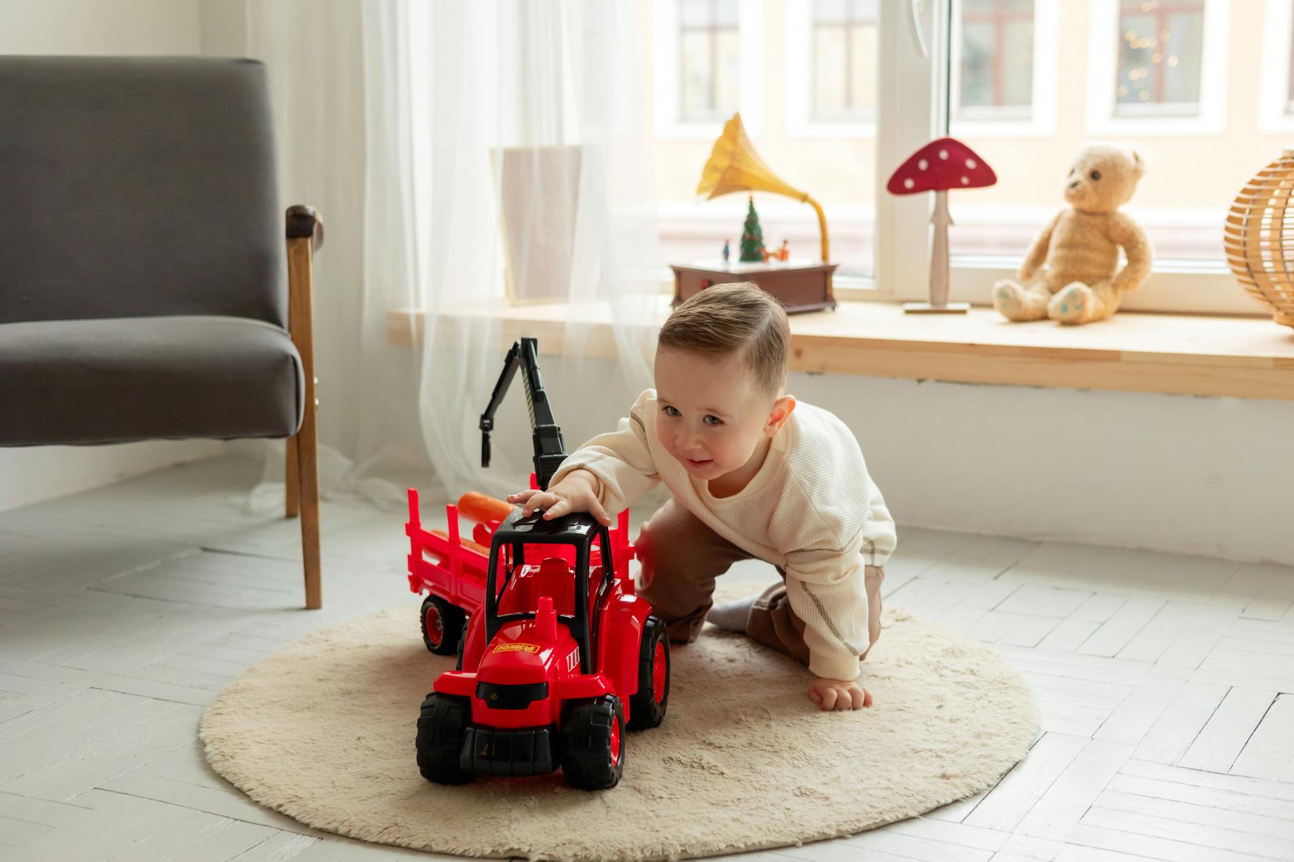 Małe dziecko bawi się czerwonym traktorkiem na dywanie w pokoju